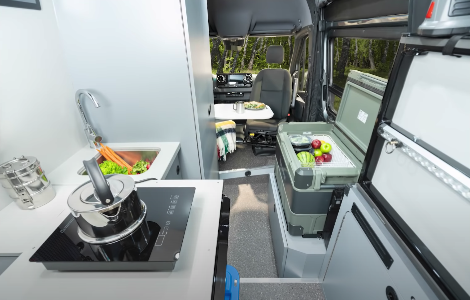 Instead of a kitchen block, the Recon 4x4 features a loose kitchen layout with bed-frame countertop, portable induction cooktop and indoor/outdoor fridge box — only the sink is part of the hard-mounted "block"