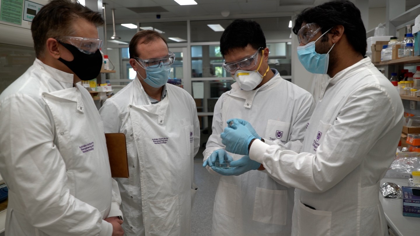 From left to right: Mr Craig Nicol (GMG), Mr Timothy Scheiwe (GMG), Dr Xiaodan Huang (AIBN) and Dr Ashok Nanjundan (GMG), standing around showing each other coin cells as if they've been asked to by a photographer
