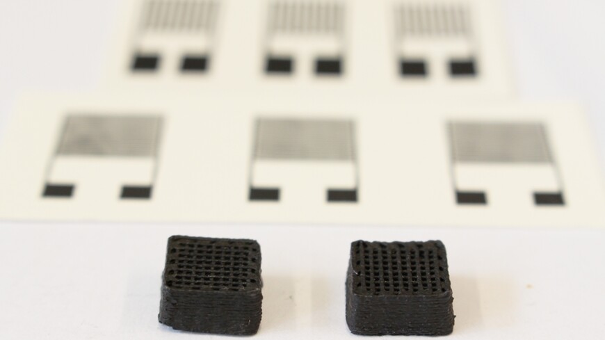 Two 3D-printed cuboids of the e-ink, each measuring 1 cm wide (printed electronic sensors can be seen in the background)