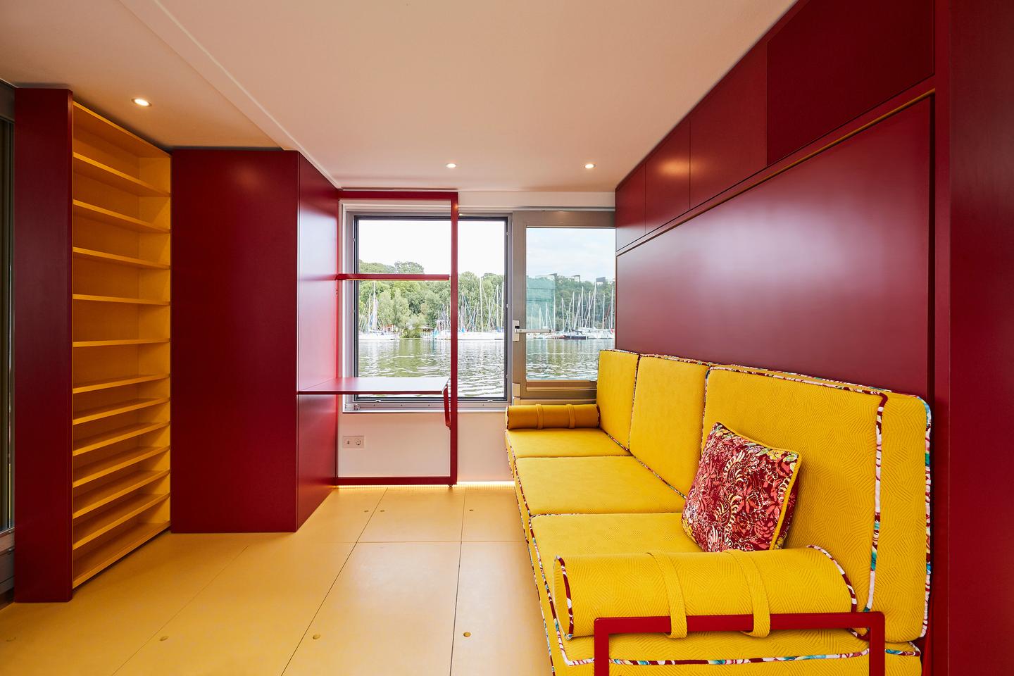 The Fàng Sōng's living room includes a large sofa bed, shelving, and a small work space overlooking a window