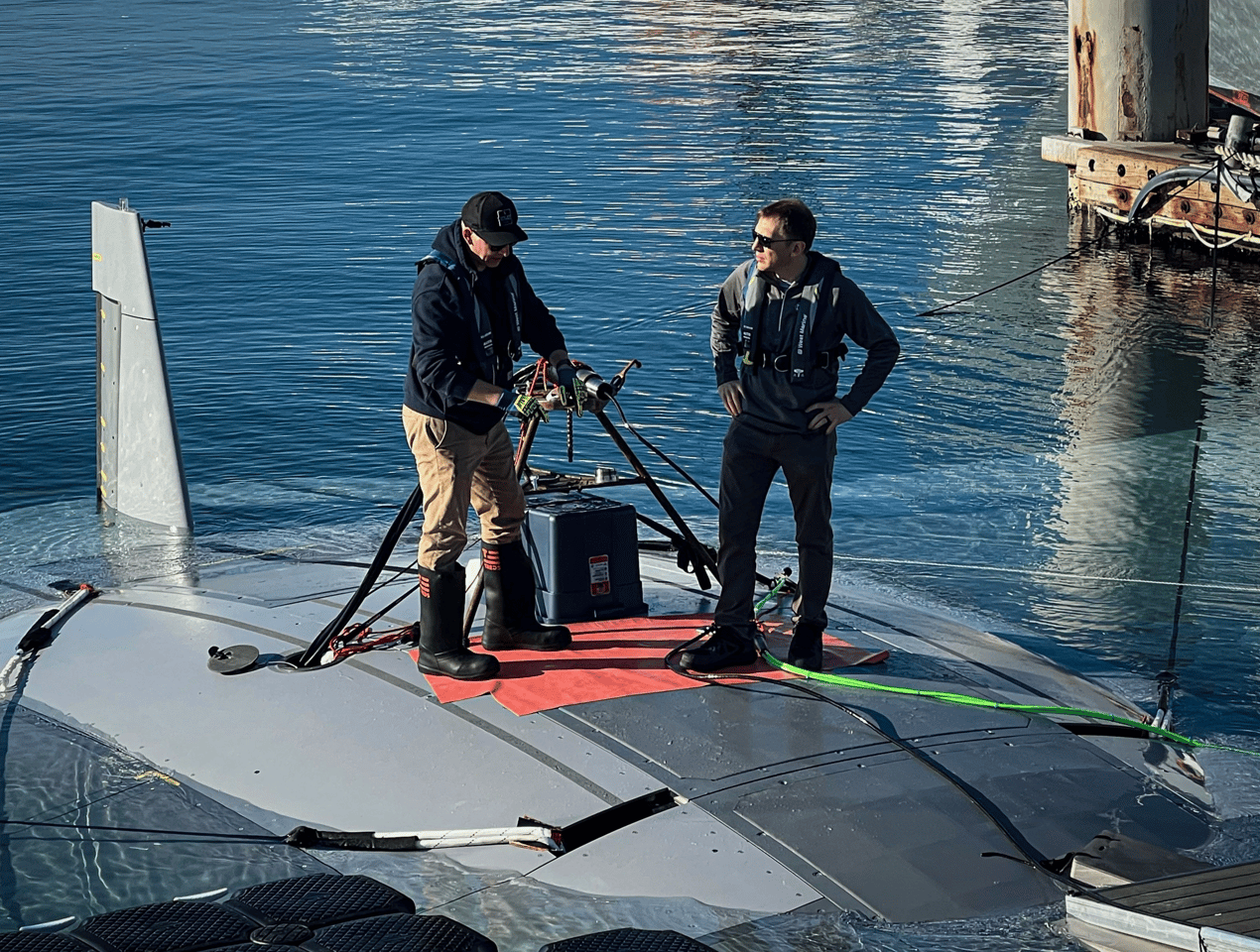 DARPA program manager Dr. Kyle Woerner (right) talks with a member of the Northrop Grumman team while standing atop the Manta Ray vehicle