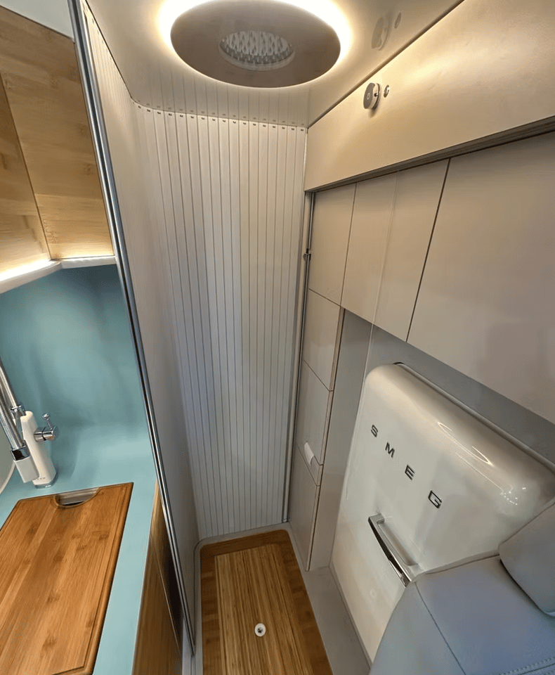 The bathroom roller door slides out from behind the cabinetry to create a private shower/toilet room; note the rainfall shower head located within the round ceiling light and the water control on the upper cabinet